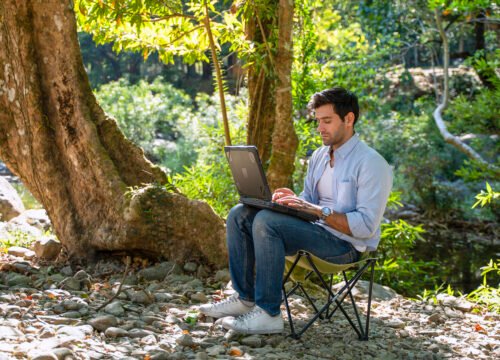White collar worker is using ragged laptop while vacation at forest. Vacation, technology.
