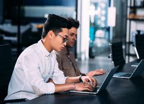 side view of multicultural businessmen working at table with laptops at modern office